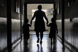 Foto de assistente social conduzindo duas crianças